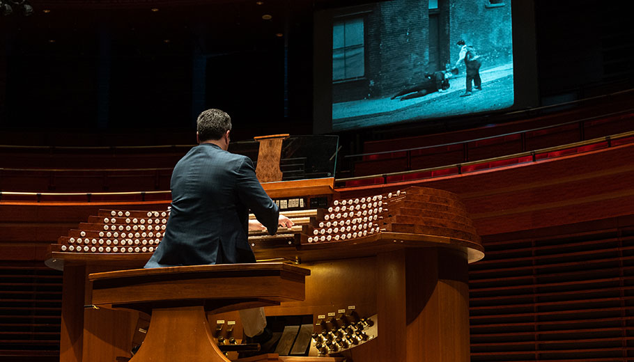 a man plays the organ while a black and white movie movie is playing on a screen