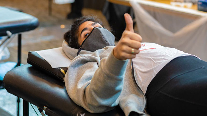 Masked Person gives thumbs as they lay down donating blood