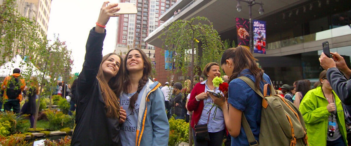 2 Women Take a Selfie in front of the greenery on Broad street at the PIFA Street Fair
