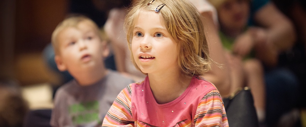 A young girl watches with rapt attention with a young boy in the background.