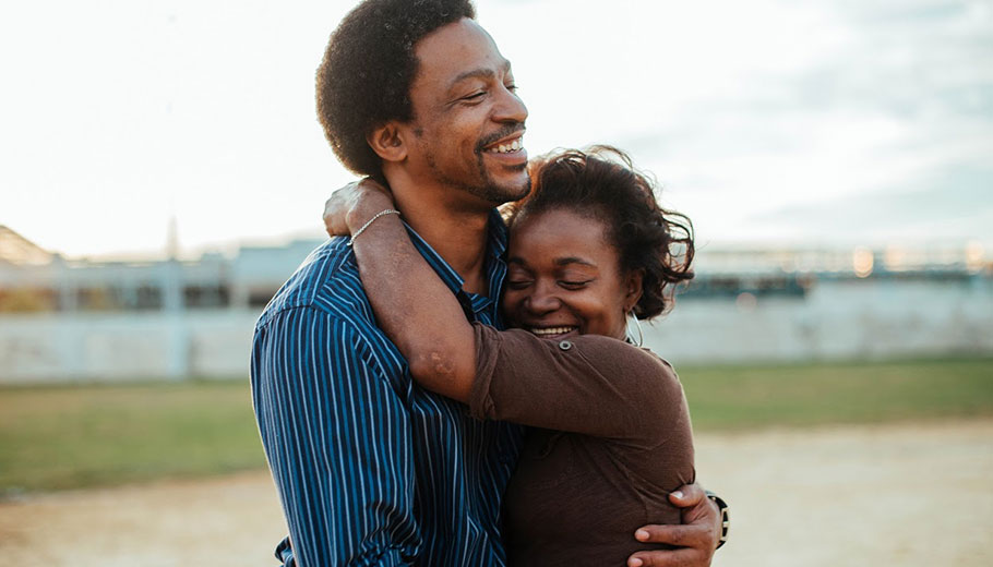 a middle age african american man and woman stand outside hugging while smiling