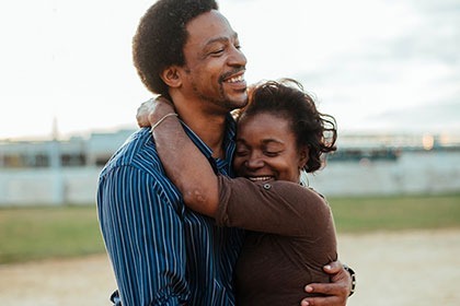 a middle age african american man and woman stand outside hugging while smiling