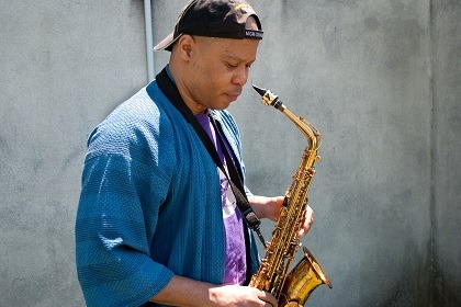 Steve Coleman Stands with alto saxophone looking down