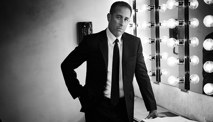 Jerry Seinfeld standing in a dressing room looking at the camera