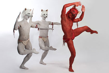 Three dancers in wolf masks - two painted white, one painted red - pose
