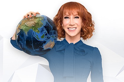 Kathy Griffin Stands in front of a white background in black shirt and pants, with  one hand on her hip and the other on her cheek with a thoughtful look