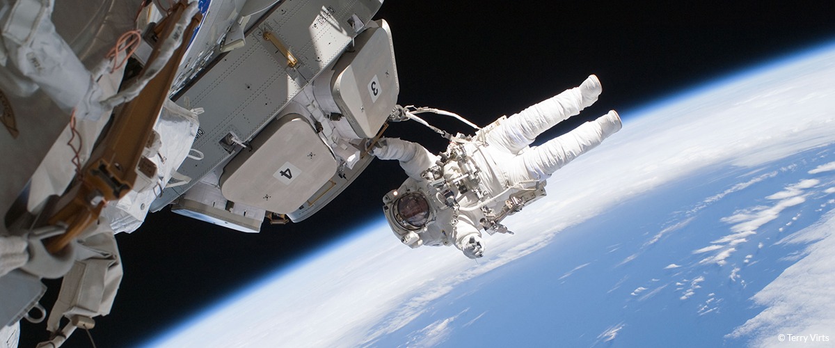 An astronaut floats outside a space vessel in space with earth in the background
