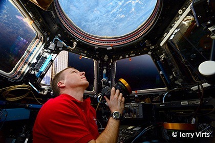 Terry Verts Looks at Earth from a spacecraft holding his camera