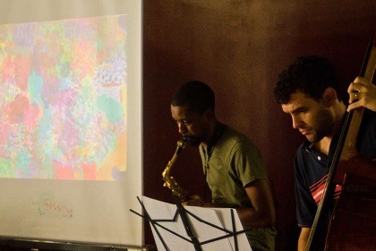 two musicians performing sax and bass with artwork projected in the background.