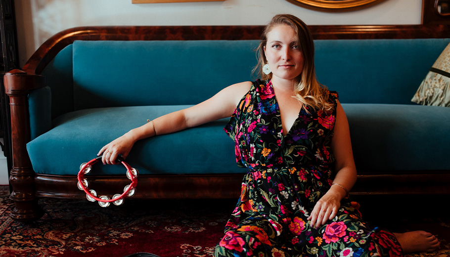 Musician  Chelsea Reed holding a tambourine and leaning against a blue couch.